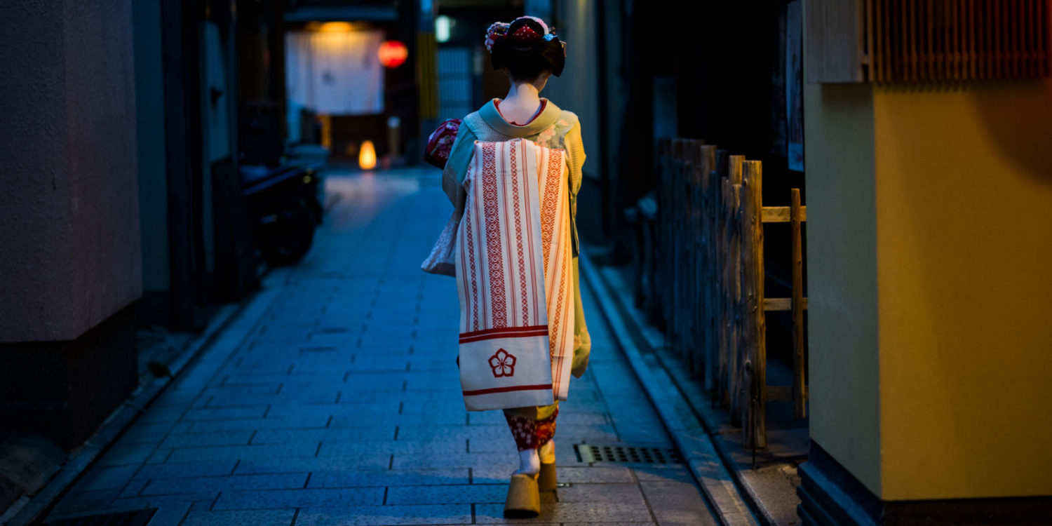 geisha o maiko de espaldas paseando por una calle a oscuras