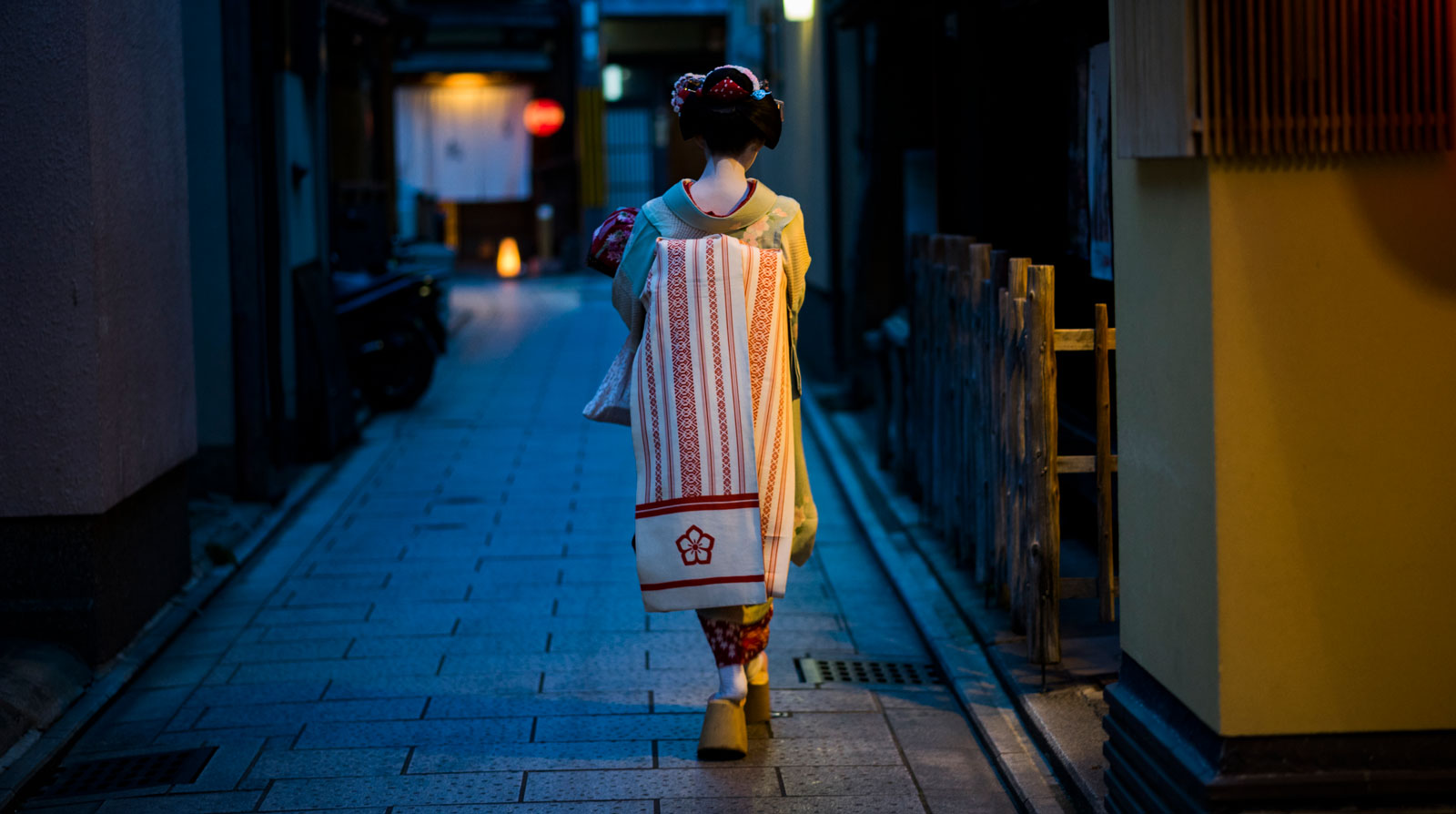 geisha o maiko de espaldas paseando por una calle a oscuras